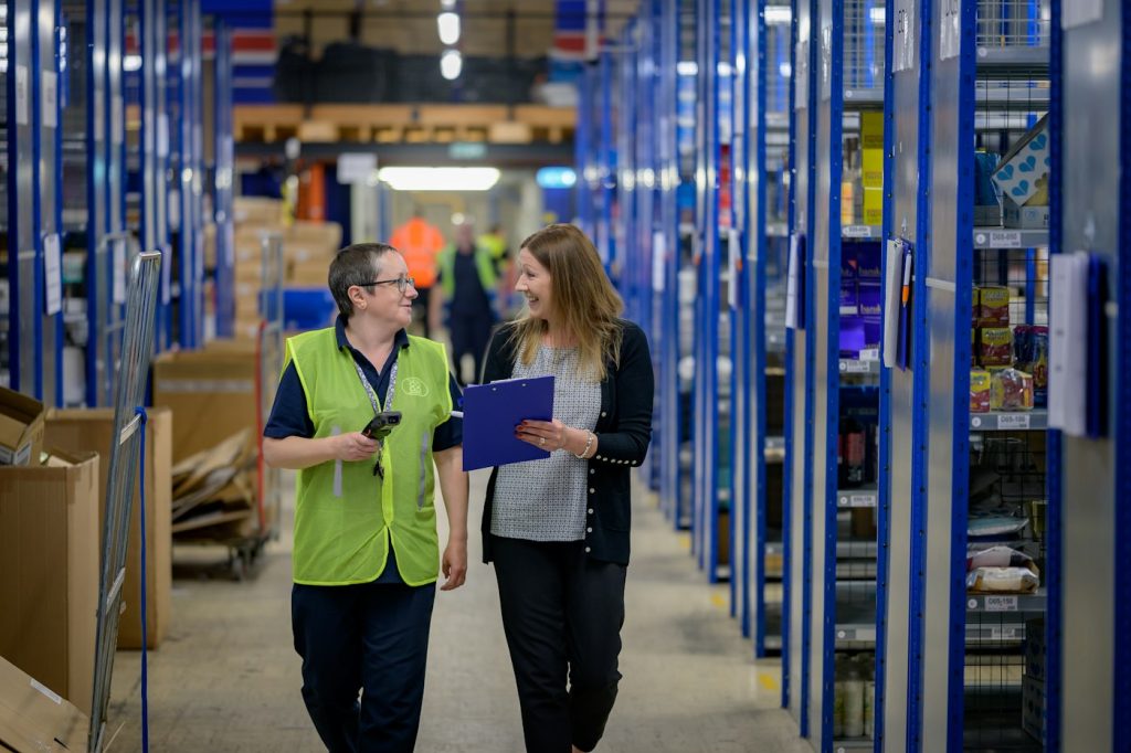 Two warehouse staff walking along shelving while checking stock on a clipboard