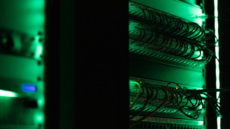 Rack of server equipment glowing in a dark room, representing cloud and shared hosting infrastructure