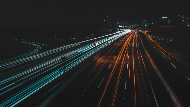 Long-exposure light trails streaking along a dark road at night, conveying speed and performance