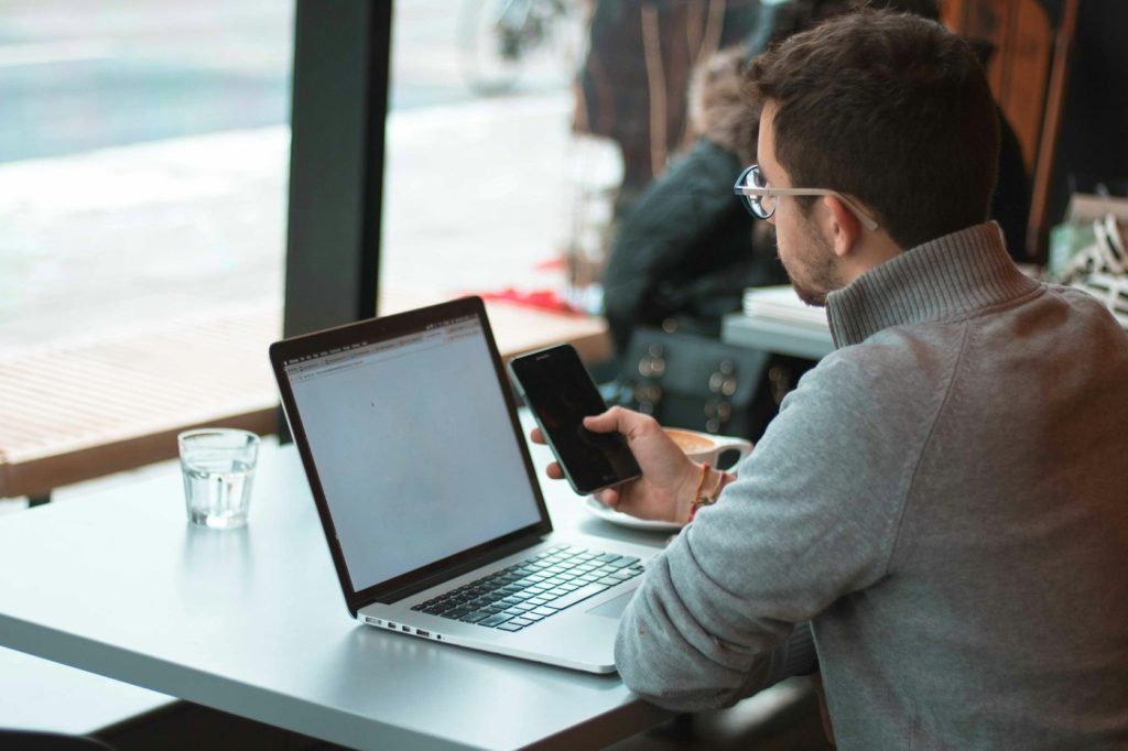 Developer working on a laptop near a window with a smartphone beside it for app testing